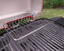 Stainless steel warming rack mounted on outdoor gas grill with black grates, garden background