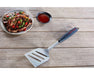 Stainless steel BBQ spatula with black handle on wooden table beside grilled steak and sauce.