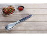 Stainless steel kitchen tongs beside grilled meat and sauce on wooden table.